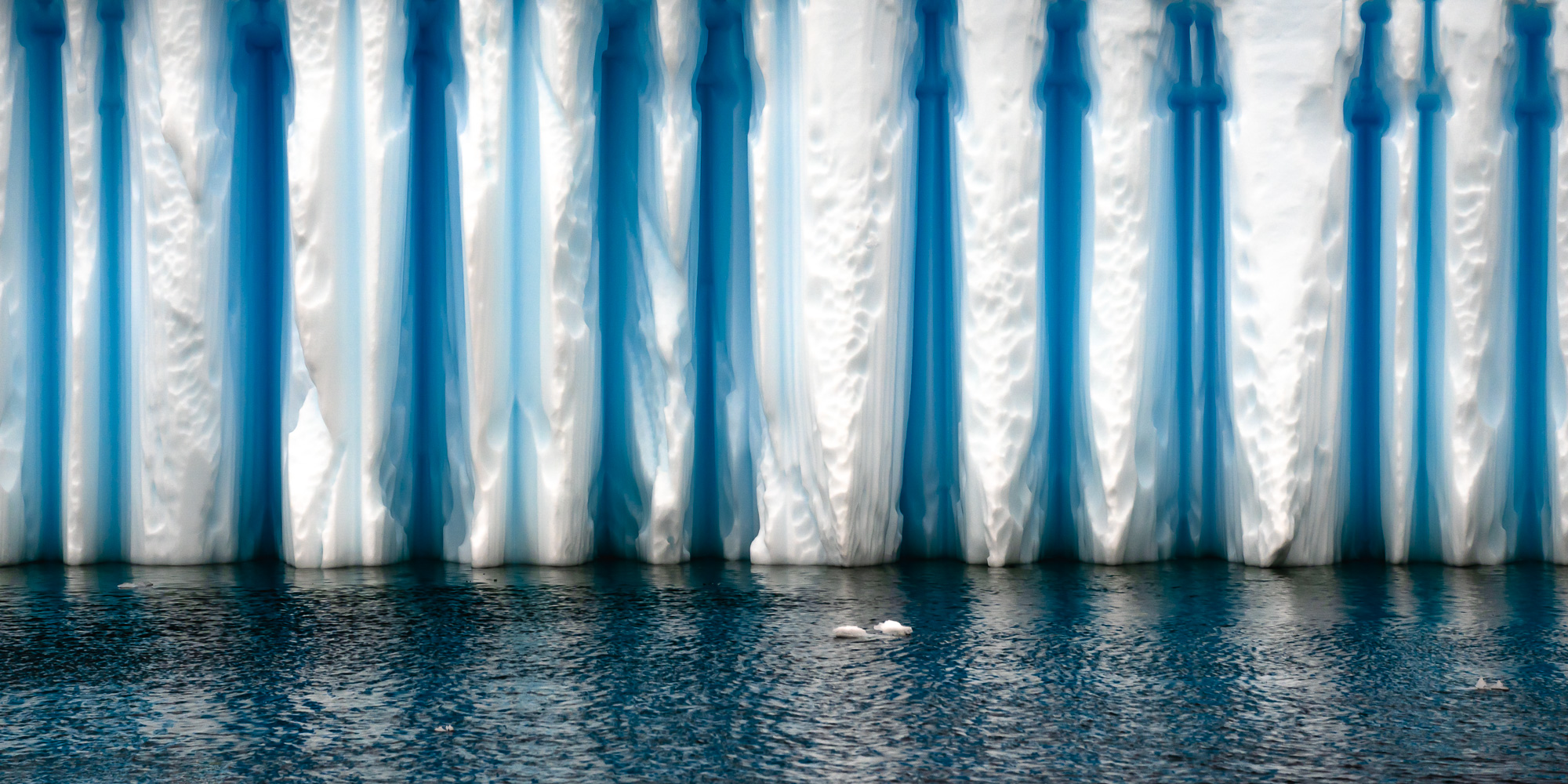 A wind carved iceberg floats near the Antarctic Peninsula. The darker blue ice is older than the lighter ice because it is compressed and contains fewer air bubbles.