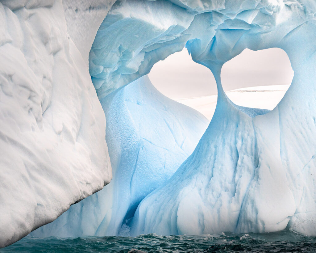 A wind carved iceberg floats near the Antarctic Peninsula. The darker blue ice is older than the lighter ice because it is compressed and contains fewer air bubbles.