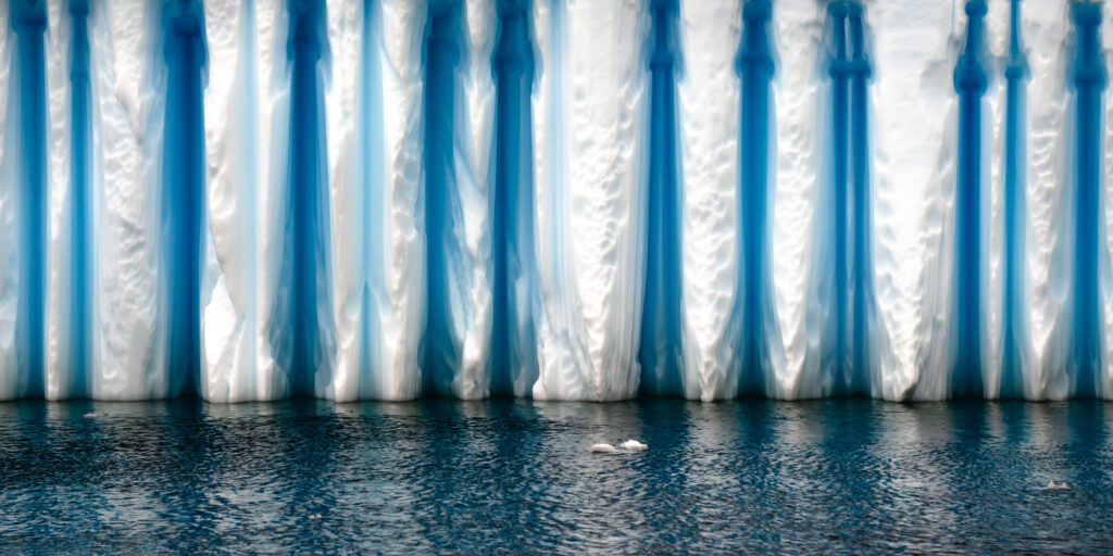 A wind carved iceberg floats near the Antarctic Peninsula. The darker blue ice is older than the lighter ice because it is compressed and contains fewer air bubbles.