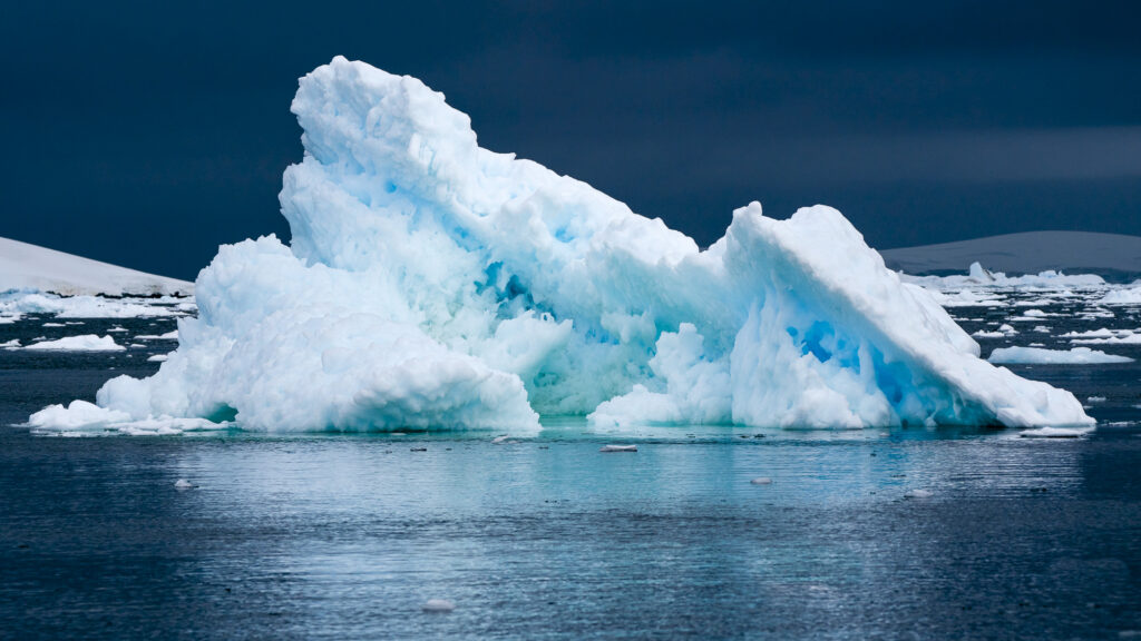 A wind carved iceberg floats near the Antarctic Peninsula. The darker blue ice is older than the lighter ice because it is compressed and contains fewer air bubbles.