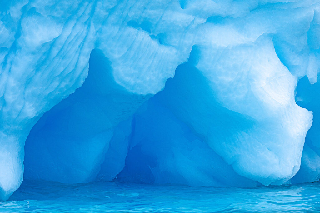 A wind carved iceberg floats near the Antarctic Peninsula. The darker blue ice is older than the lighter ice because it is compressed and contains fewer air bubbles.