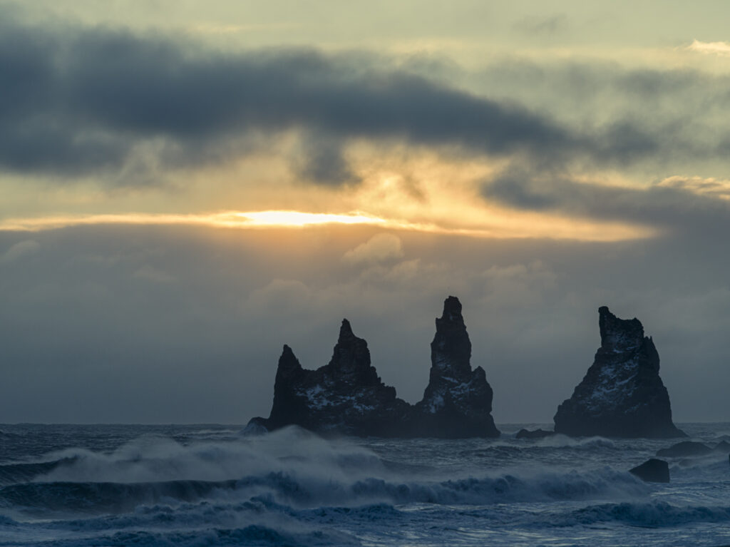 The setting sun bursts through the winter clouds and add a sense of drama to the Reynisdrangar rock formation on Iceland's southern coast.