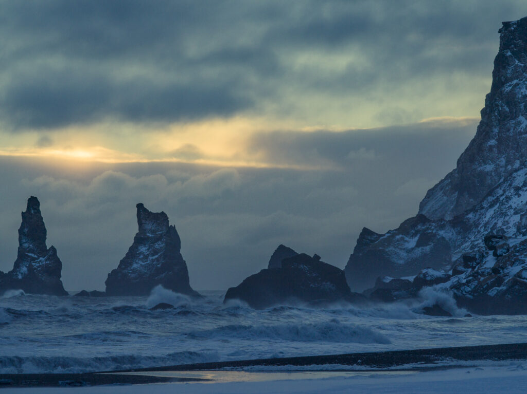 The setting sun bursts through the winter clouds and add a sense of drama to the Reynisdrangar rock formation on Iceland's southern coast.