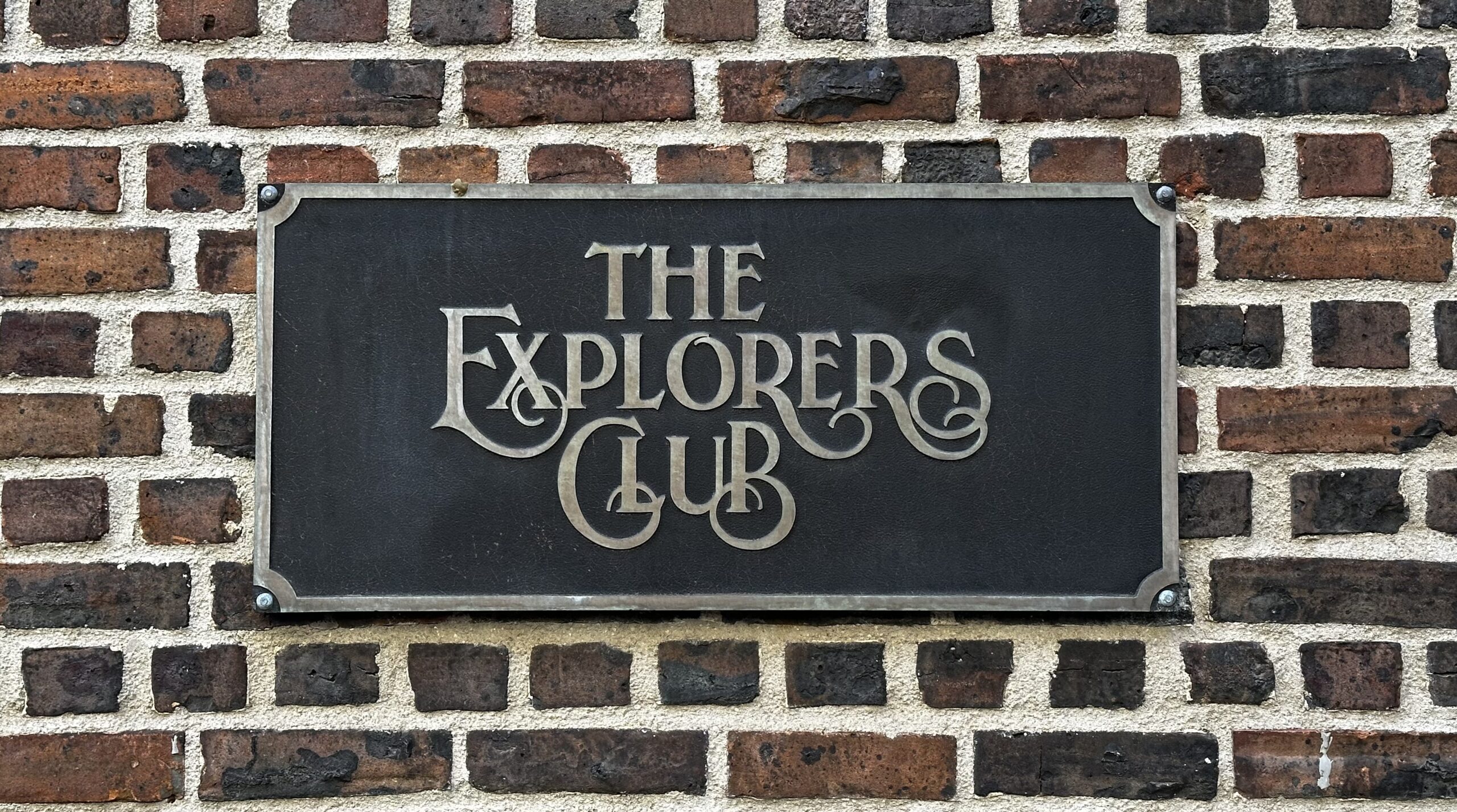 "The Explorers Club" plaque on brick wall, wide view.